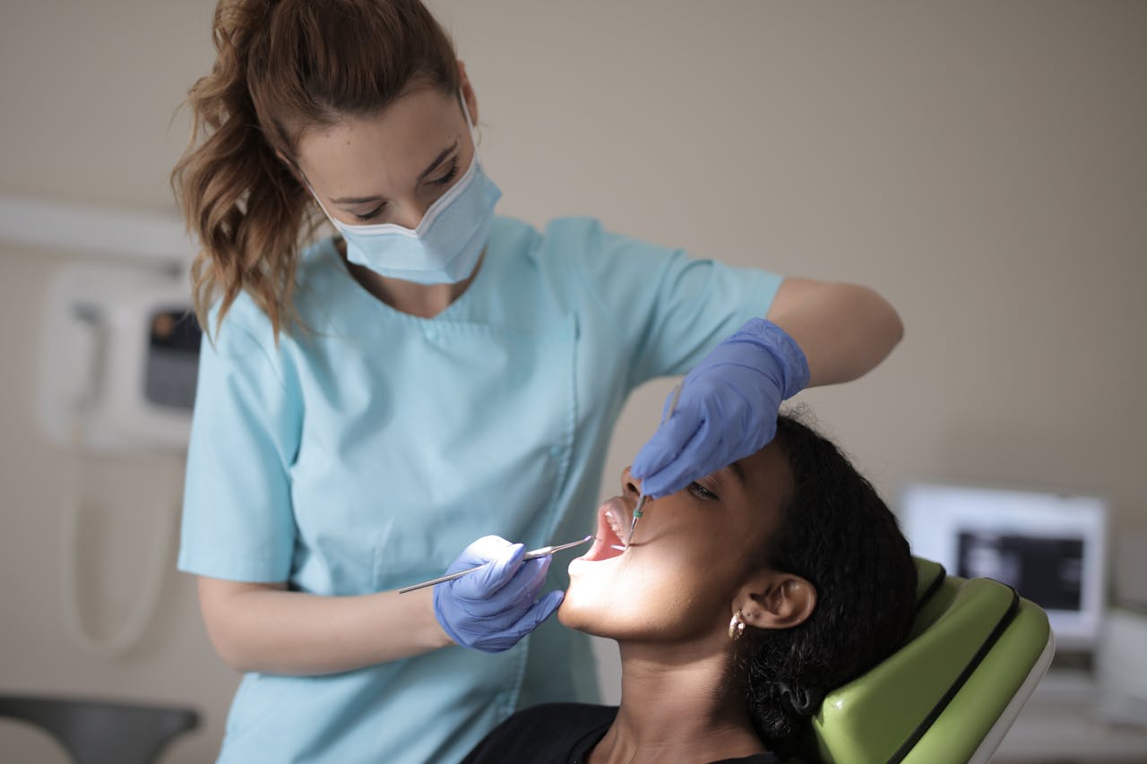 Dentist in blue scrubs and mask examines patients teeth in clinic setting.