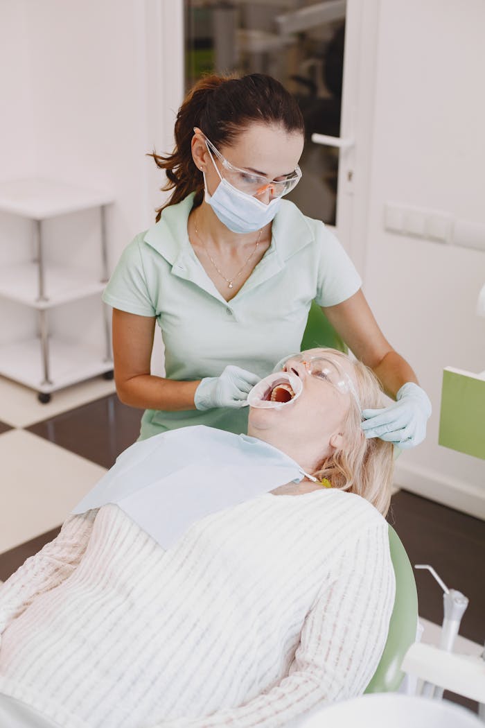 Dentist in protective gear treats patient in a modern clinic, ensuring safe dental care.